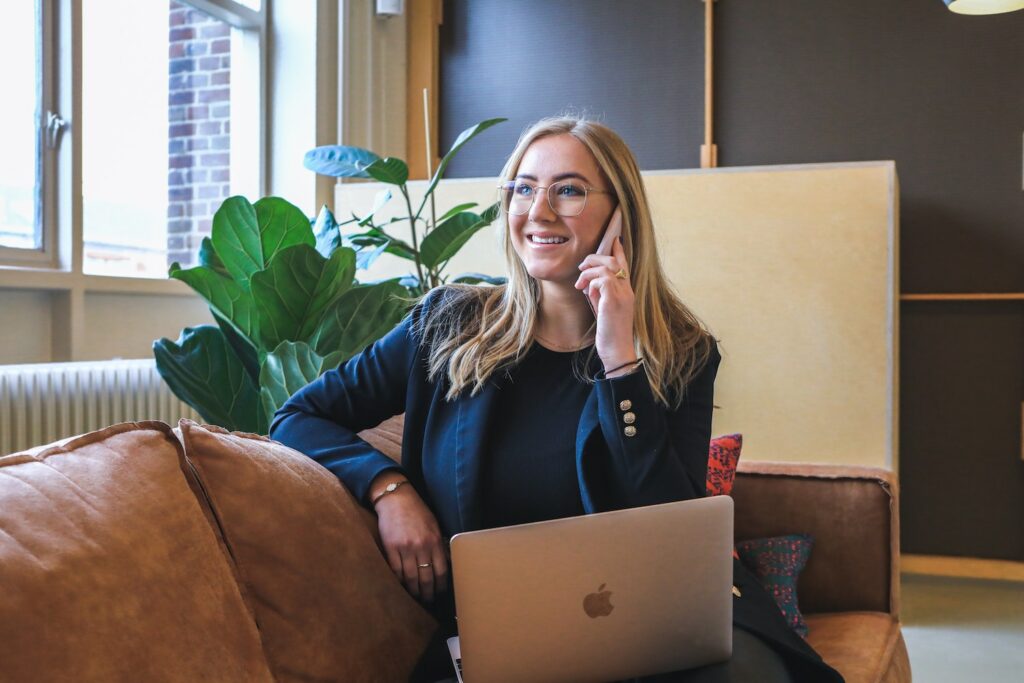 Woman on the phone sitting on a couch with a Macbook