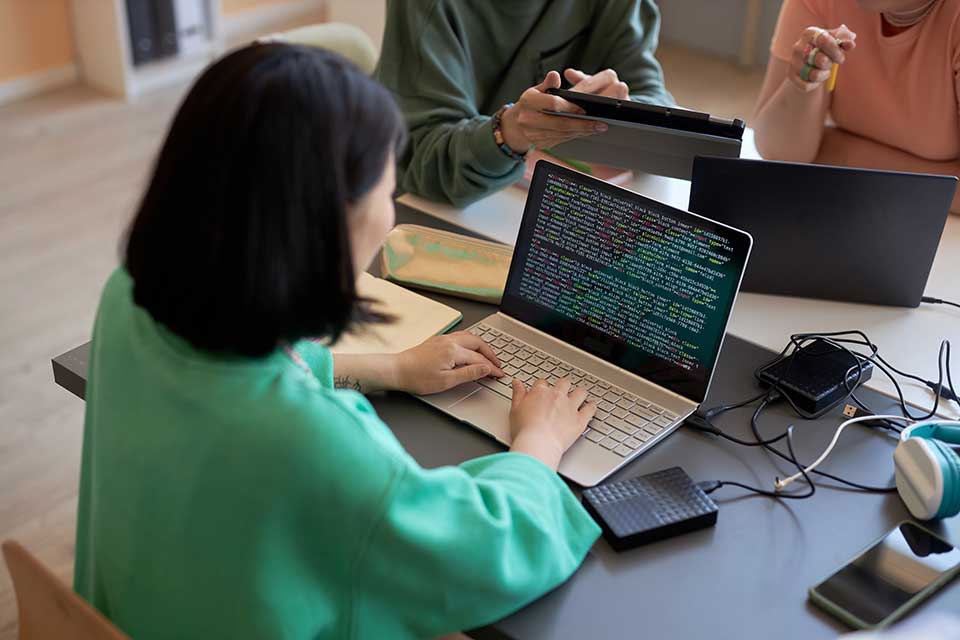woman coding on laptop at desk with others