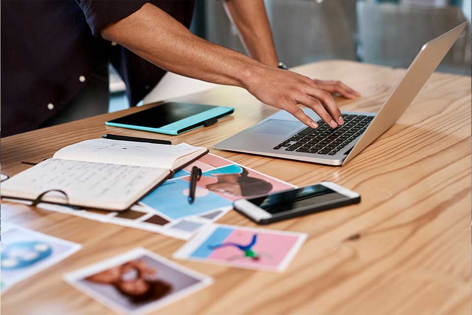 person using laptop on desk with documents scattered across it