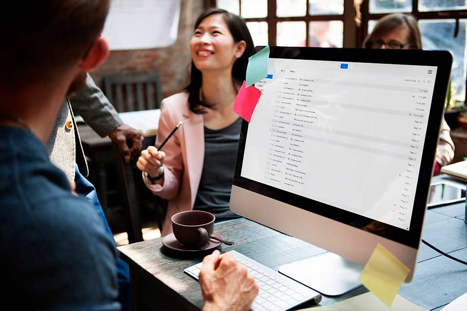 group of people at desk while emails are visible on computer screen